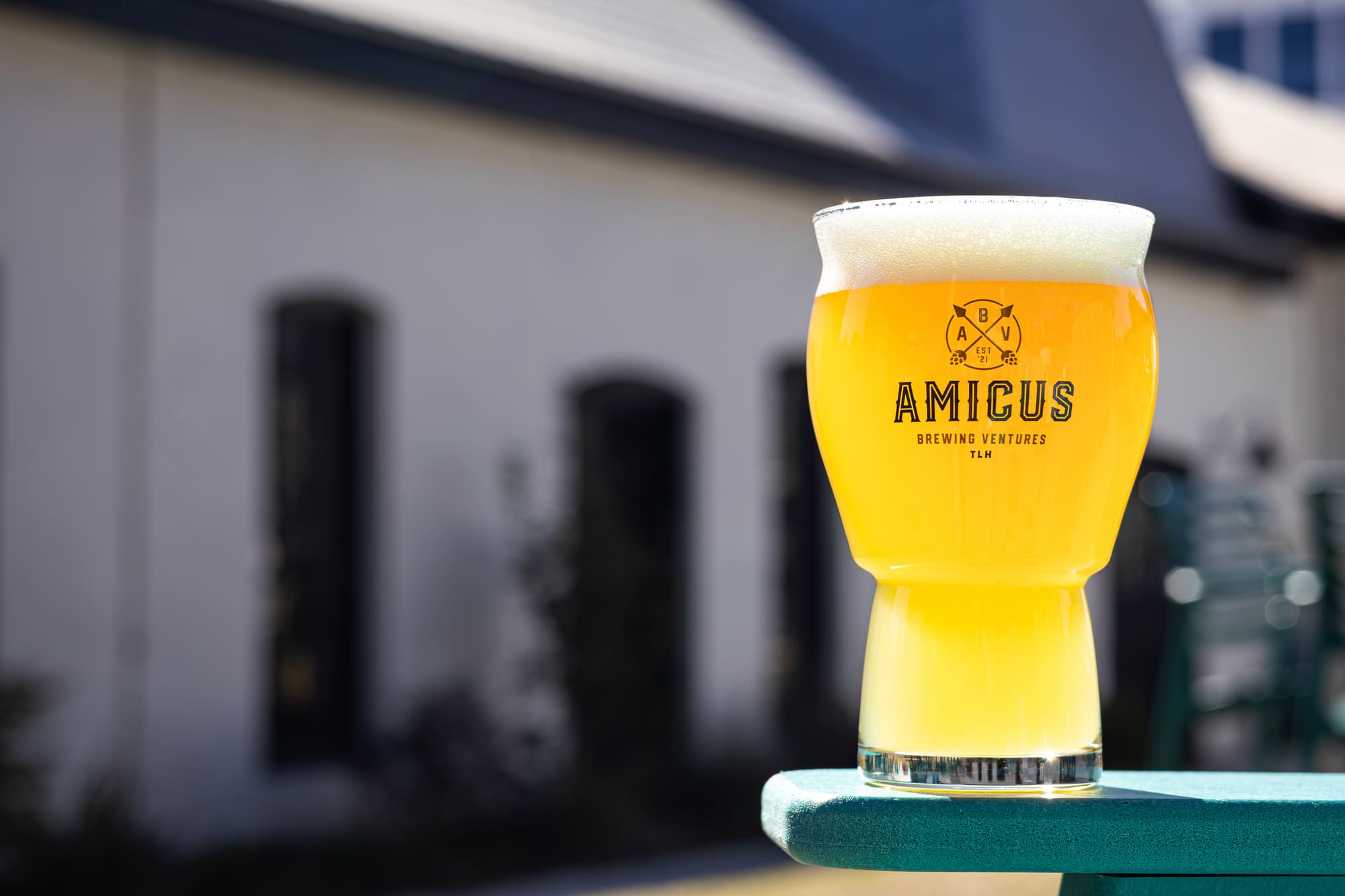 A pale hazy beer on a teal table outside the brewery.