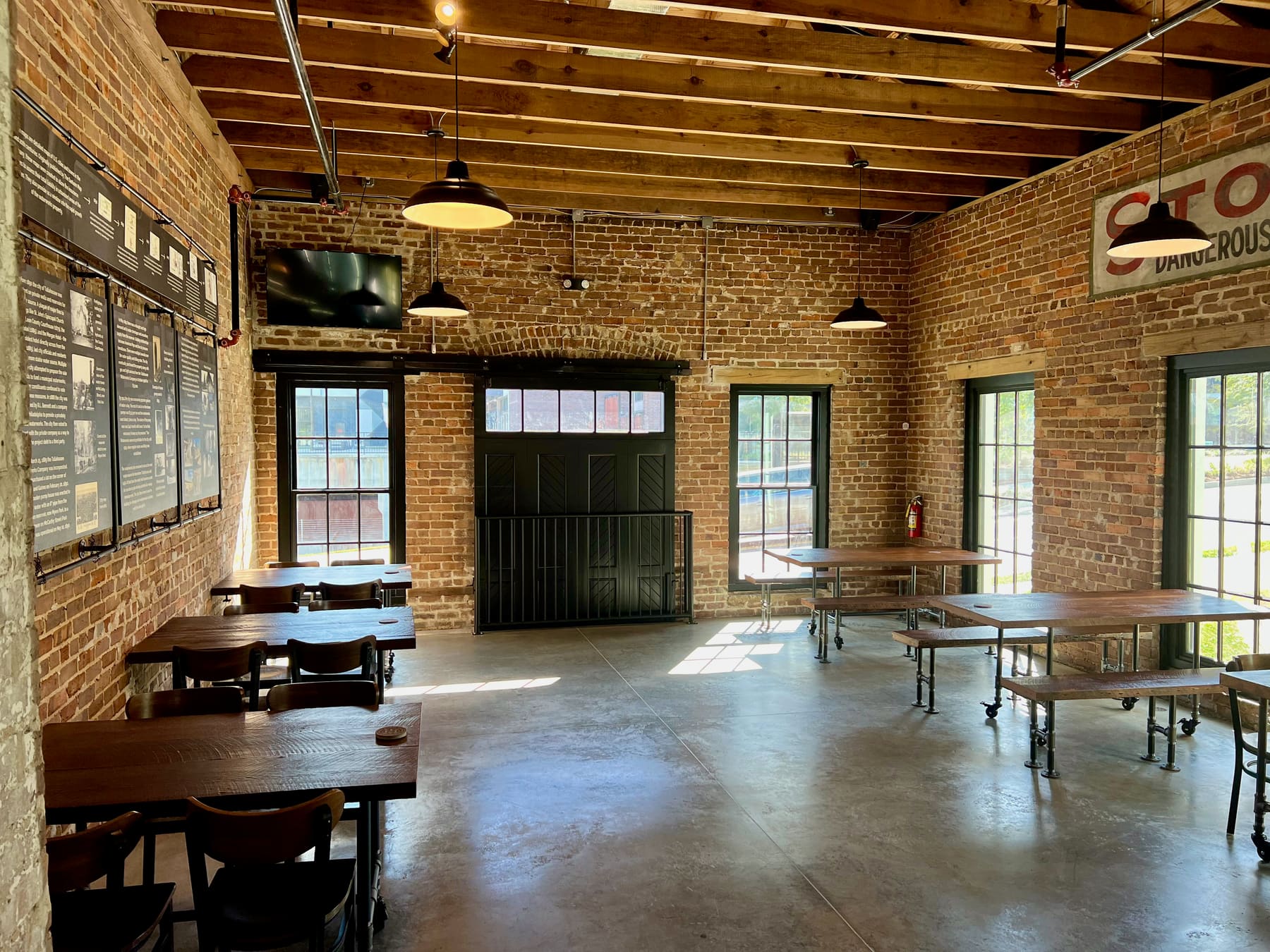 The Wellhead: a brick room with a timber ceiling, long wooden tables, a television and tall windows on two sides.